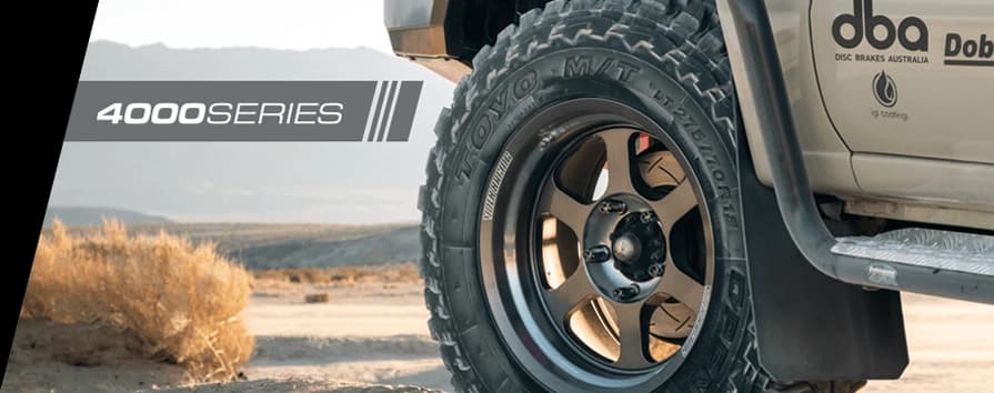 Nahaufnahme 4WD-Fahrzeugrad auf Wüstenterrain mit DBA 4000 Series Branding prominent auf Fahrzeugkarosserie sichtbar, zeigt Offroad-Bremsleistung