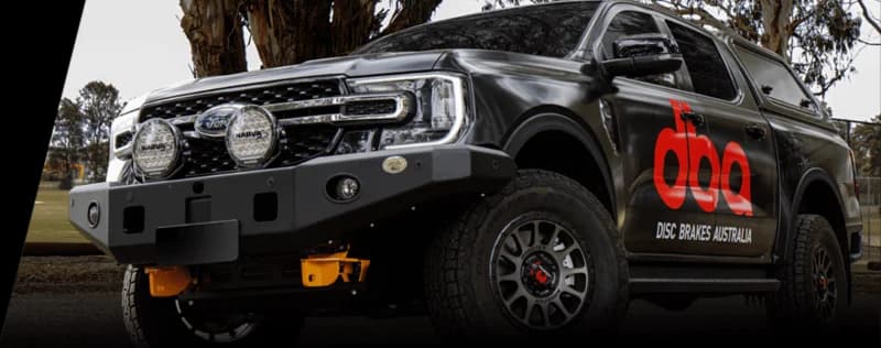 DBA Disc Brakes Australia gebrandeter dunkler Pickup-Truck mit rotem DBA-Logo und zusätzlicher Beleuchtungsausrüstung in Außenumgebung