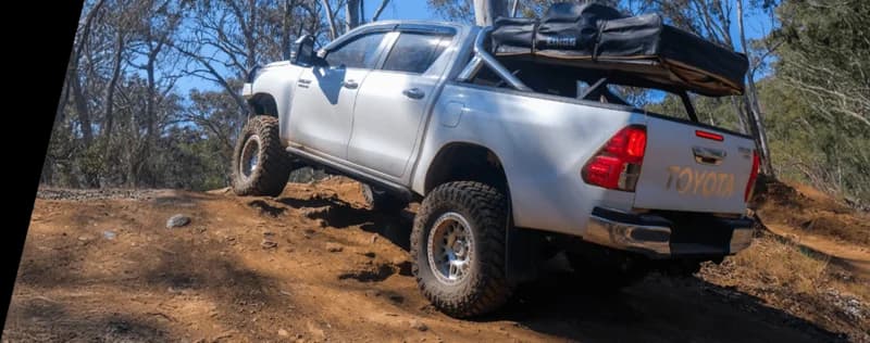 Weißer Toyota Pickup-Truck beladen mit Campingausrüstung positioniert auf felsigem Gelände in australischem Busch demonstriert schwere Last Offroad-Bedingungen