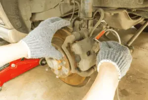 Richtige Technik zum Öffnen des Bremssattelentlüftungsventils mit Schraubenschlüssel und Auffangschlauch während der Entlüftung Behandschuhte Hände eines Mechanikers öffnen das Bremssattelentlüftungsventil mit Schraubenschlüssel während ein Schlauch angebracht ist