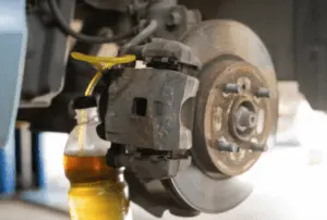 Bremsflüssigkeit und Luftblasen werden durch das Entlüftungsventil in den Auffangbehälter während der korrekten Entlüftungssequenz ausgestoßen Bremssattel mit gelbem Auffangschlauch am Entlüftungsventil, der bernsteinfarbene Bremsflüssigkeit in einen klaren Behälter während der Entlüftung zeigt