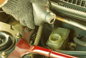 Nachfüllen von Bremsflüssigkeit im Hauptbremszylinderbehälter, um Lufteintritt während des Bremsentlüftungsprozesses zu verhindern Behandschuhte Hand eines Mechanikers gießt frische Bremsflüssigkeit in den Hauptbremszylinderbehälter während der Entlüftungsprozedur
