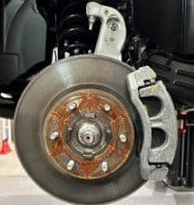 Schritt 1A: Originalbremsanlage mit Bremsscheibe und Bremssattel, die während der DBA-Bremsaufrüstung ersetzt werden Nahaufnahme der Originalbremsanlage mit verrosteter Scheibenoberfläche, Bremssattel und Halterung vor der DBA-Bremsaufrüstung